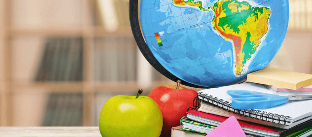 A globe, apples, and school supplies on a desk in a classroom setting.