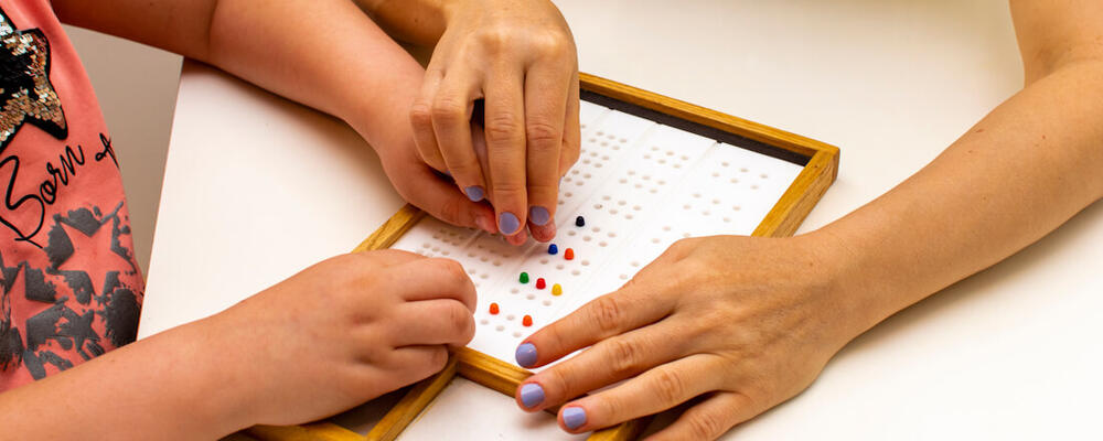 A child and an instructor use a tactile board with colorful pegs during a special education lesson.
