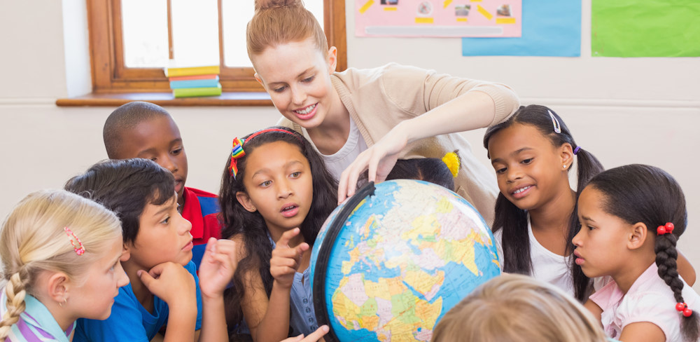 Children pointing at a globe with their teacher